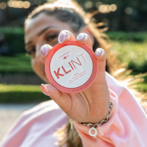 Woman wearing pink holding KLINT nicotine pouch in pomegranate flavour